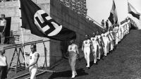 2984351 Team entry of gymnasts, Olympic Games Berlin 1936 (b/w photo); (add.info.: Berlin, Berlin/City State, Germany
The national teams of gymnasts (in the foreground the German national team) enter, accompanied by the music of a trumpet corps, behind the national flags (in front the swastika flag, in the background the Czechoslovak) in the Dietrich-Eckart-Buehne, a gymnastics venue. Above the scoreboard can be seen.); © SZ Photo.