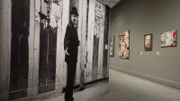 Salle grise avec une grande photographie en noir et blanc d’un homme devant un mur d’affiches et des affiches lacérées accrochées – exposition « Paris à l’arraché. Jacques Villeglé et l’art urbain », musée Carnavalet, Paris